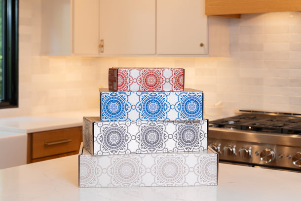 Two closed Terlato Kitchen gift boxes with charcoal and white patterns on a kitchen counter.