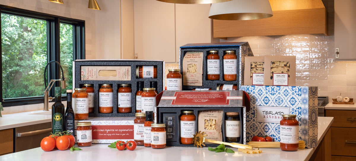 Open Terlato Kitchen gift boxes with pasta, sauces and biscotti beside blue-and-white gift packaging.